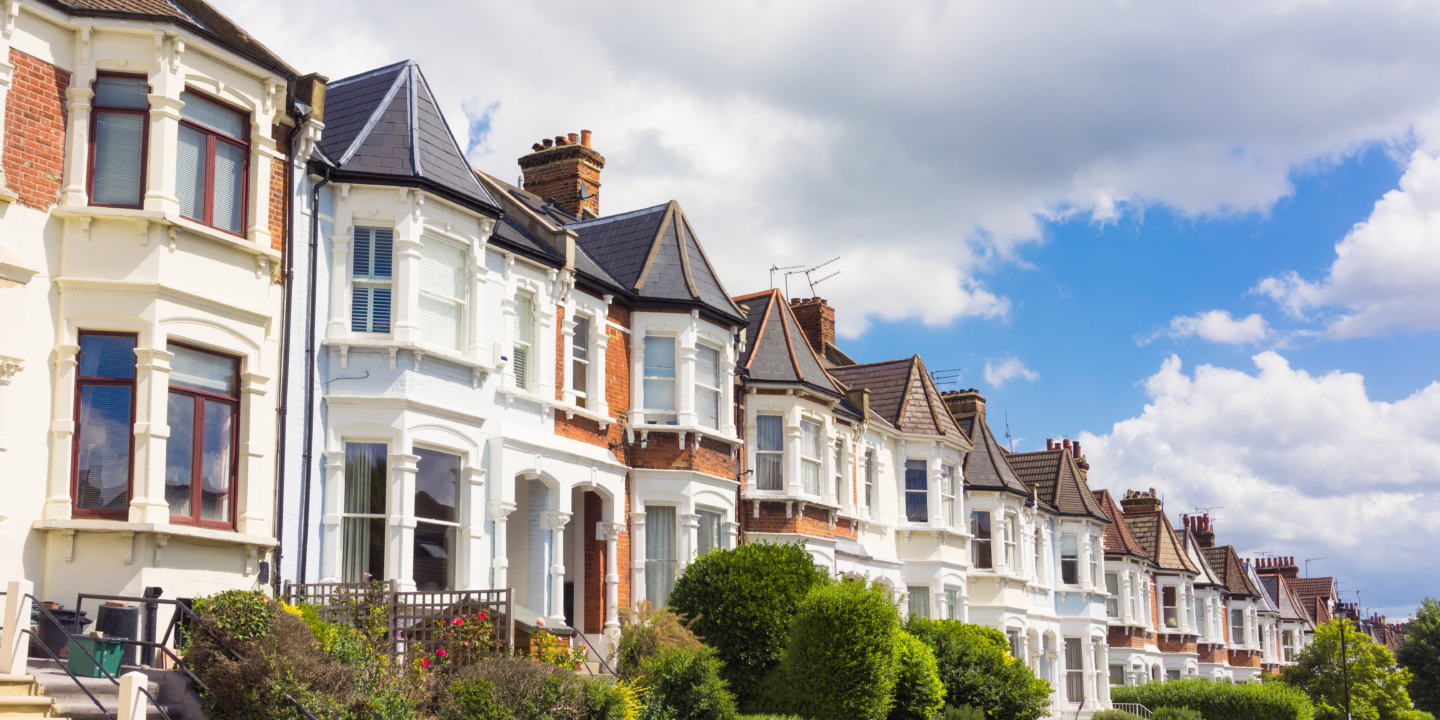 A row of terraced houses with white and red brick facades under a blue sky with fluffy clouds.