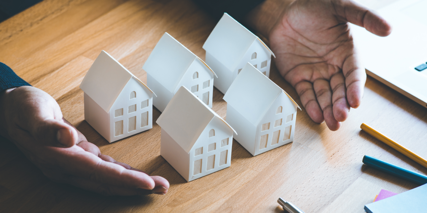 A person's hands framing five small model houses on a wooden table.