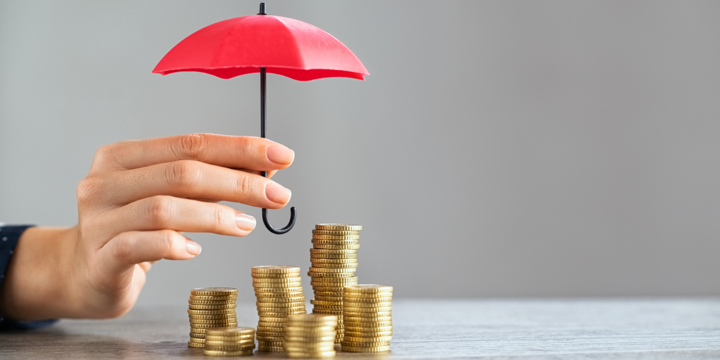 A person shelters stacks of coins with an umbrella, symbolizing protection of wealth and financial security.