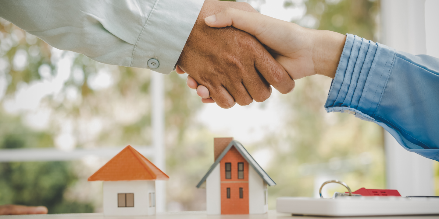 Two individuals shaking hands over a model house, symbolizing a successful real estate agreement or partnership.