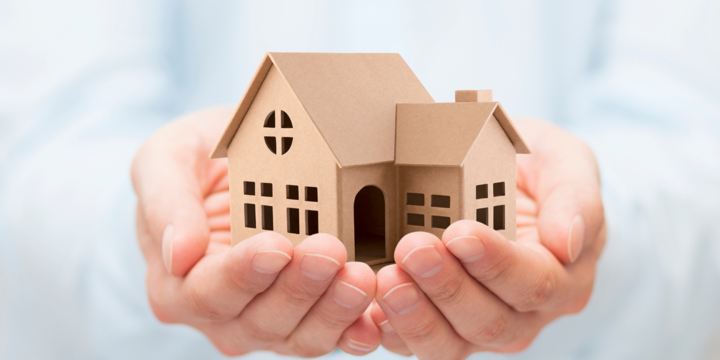 A person gently holds a small cardboard house