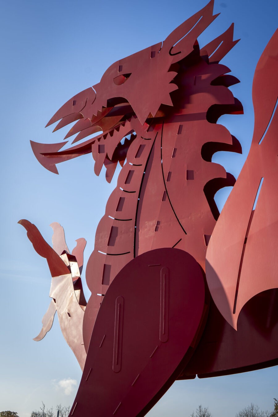 A stylised red metal sculpture of the Welsh dragon against a clear blue sky.